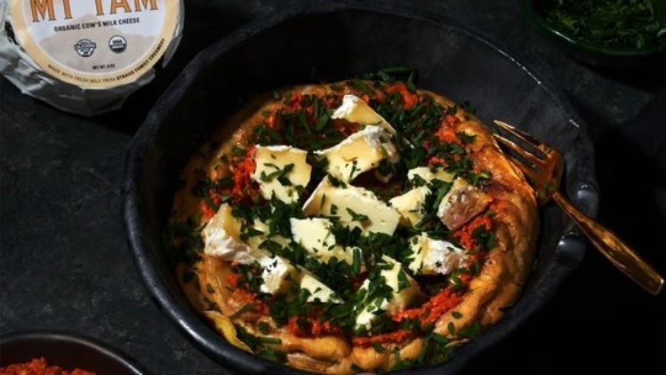Mt Tam Dutch baby topped with roasted red pepper sauce, melted triple cream cheese, and fresh herbs, creating a rich and savory brunch centerpiece.