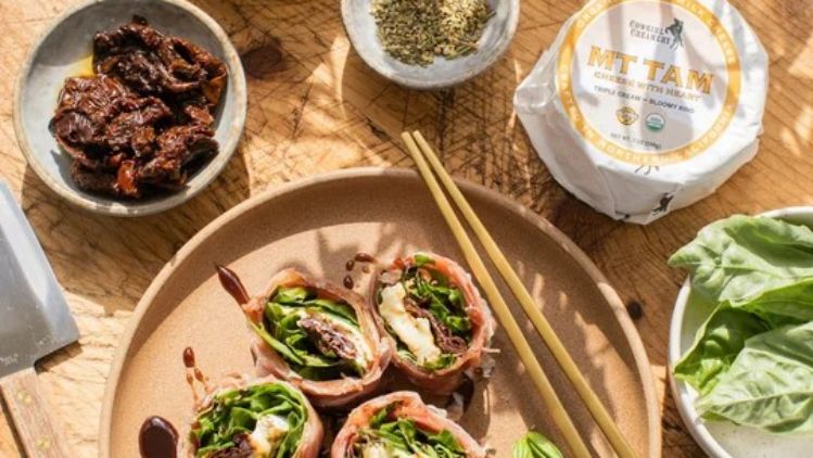 Prosciutto-wrapped Mt Tam rotolo filled with fresh basil, leafy greens, and sun-dried tomatoes, served with a rich balsamic glaze for an elegant appetizer.