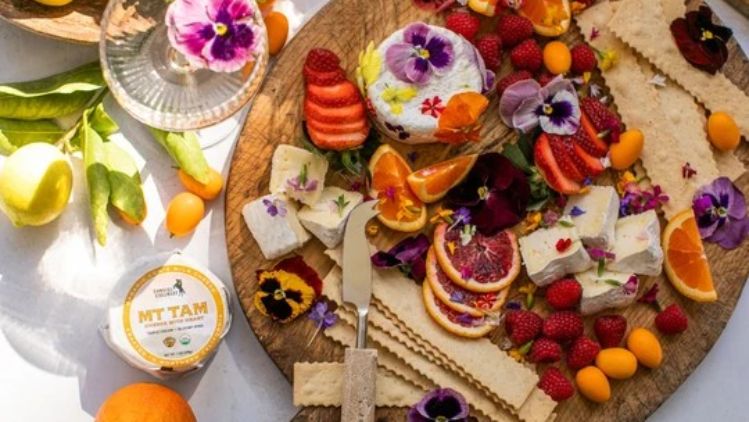 Elegant Mt Tam cheese board featuring edible flowers, fresh berries, citrus, artisan crackers, and creamy triple cream cheese for a colorful and sophisticated entertaining spread.