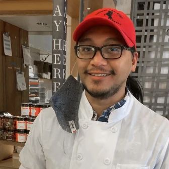Artisan cheesemaker in a creamery shop, sharing expertise and showcasing handcrafted cheeses in a welcoming retail setting.