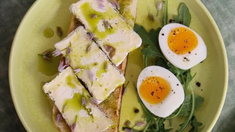 Pierce Point cheese toast topped with olive oil and edible flowers, served alongside soft-boiled eggs and fresh arugula for an elegant breakfast or brunch.
