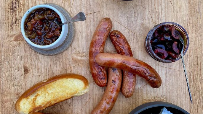 Grilled frankfurters served with creamy Mt Tam cheese, toasted buns, whole-grain mustard, caramelized onion jam, and pickled cherries for a gourmet twist on a classic meal.