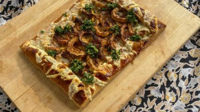 Rustic delicata squash galette topped with artisan cheese and fresh herb pesto, baked on a golden flaky crust for a flavorful seasonal dish.