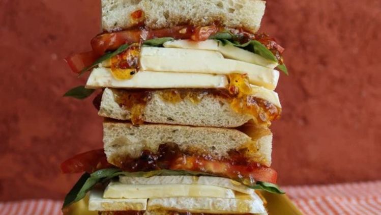 Mt Tam sandwich layered with ripe tomatoes, fresh basil, pepperoncini, and creamy triple cream cheese on rustic bread for a rich and flavorful lunch.