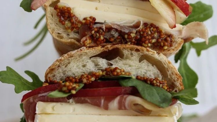 Mt Tam sandwich layered with ripe tomatoes, fresh basil, pepperoncini, and creamy triple cream cheese on rustic bread for a rich and flavorful lunch.