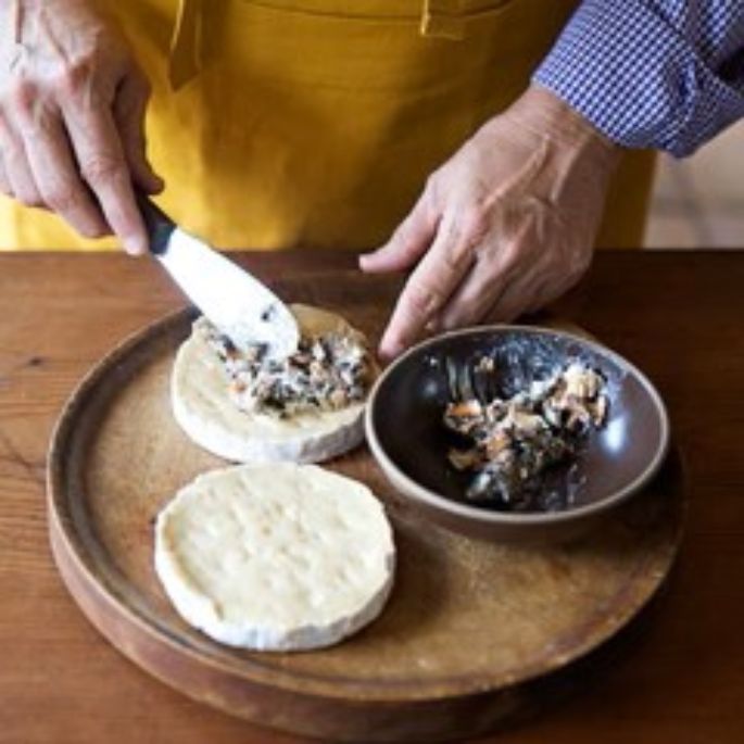 Mt Tam or Camembert cheese being carefully layered with truffles or wild mushrooms to create a rich and elegant gourmet appetizer.