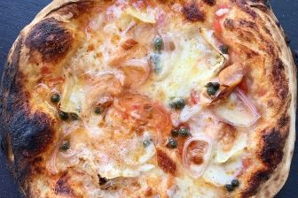 Wood-fired pizza topped with melted artisan cheese, smoked salmon, capers, and shallots, baked to a perfectly crisp golden crus