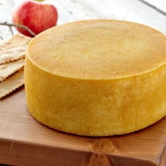 Hop Along artisan cheese wheel displayed on a wooden board, showcasing its natural golden rind and handcrafted farmstead character.