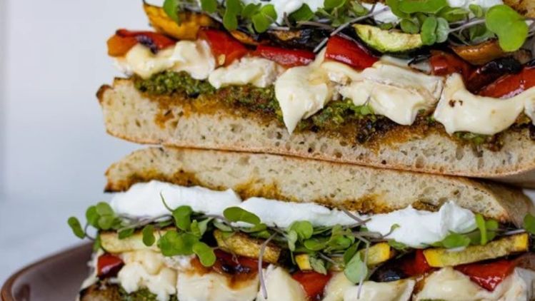 Grilled vegetable sandwich with creamy Mt Tam triple cream cheese, pesto, roasted zucchini, peppers, and microgreens layered on artisan bread